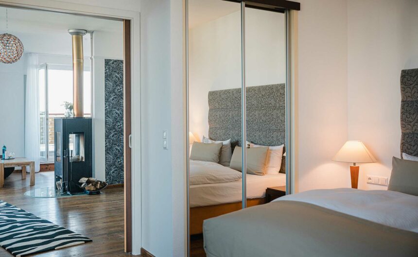 Blick vom Schlafbereich einer Suite mit Doppelbett in einen offenen Wohnbereich mit Kamin.