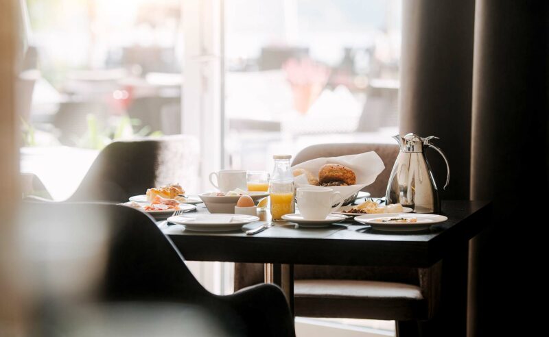 Nahaufnahme auf gedeckten Frühstückstisch mit Kaffee und Säften, im Hintergrund die Außenterrasse.